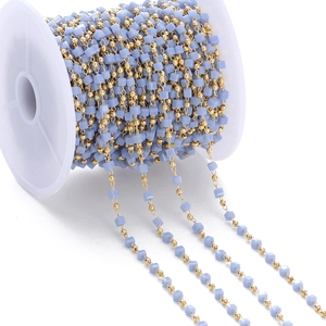 Detail of gold bead chain with light blue square beads wrapped on white spool