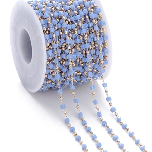 Detail of light blue square crystal beads and gold round beads on a white spool