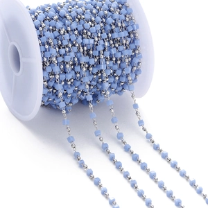 Detail of light blue cubic faceted beads and silver ball chain wound on a white spool