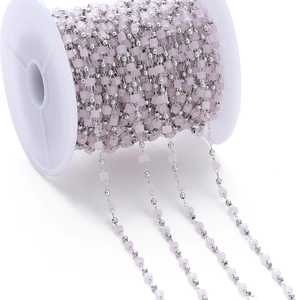 Detail of pink crystal cube and silver bead chain on white spool for DIY jewelry