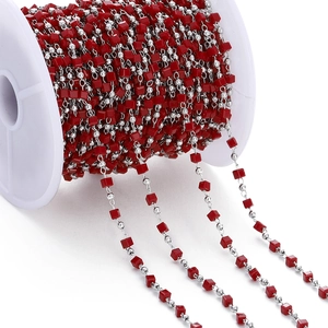 Detail of DIY chain with red cube beads and silver round beads on a white plastic spool