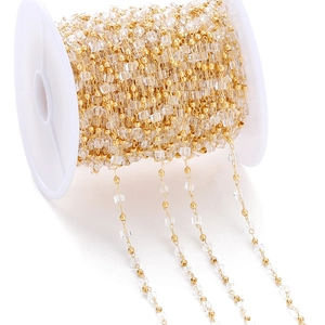 Macro shot of gold beads and clear crystal chain on white spool for jewelry making