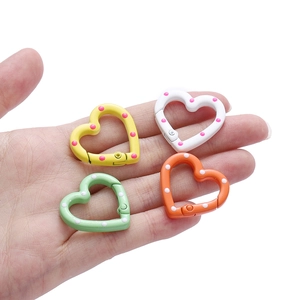 Hand holding four colorful heart-shaped spring ring buckles with polka dot metal finish