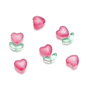 Dettaglio di perle in vetro a cuore rosa e foglia verde per creazione gioielli fai-da-te