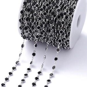 Detail van zwarte zirkonia's in zilveren metalen ketting op witte spoel voor DIY sieraden maken