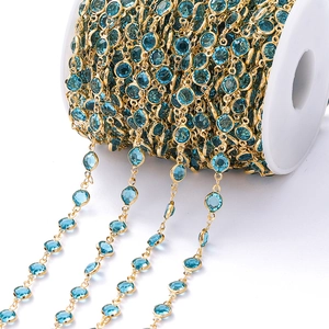 Detail van een 1m vergulde koperen ketting met blauwe zirkoon op een witte spoel