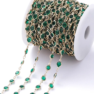 Detail van gouden ketting met gefacetteerde groene zirkoonkralen op een witte spoel DIY