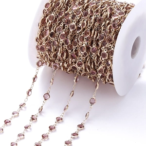 Detail van een 1m lange vergulde koperen ketting met paarse zirkoonstenen op een spoel