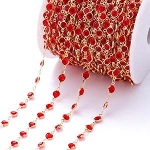 Detail van vergulde koperen ketting met rode geslepen zirkonen op een witte plastic spoel