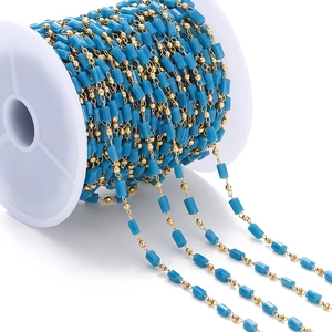 Detalle de cuentas cilíndricas azules y cadena dorada en carrete blanco para joyas DIY