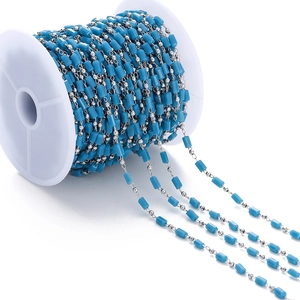Detalle macro de cuentas cilíndricas azul cielo y cadena de plata en un carrete