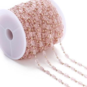 Detalle de cuentas de cristal rosa y eslabones dorados en un carrete de plástico