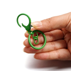 Chiusura a moschettone verde erba opaca con anello portachiavi tenuto in mano su bianco