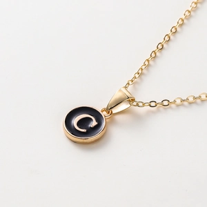 Détail macro du collier doré avec pendentif en émail noir orné d'une lettre C en relief
