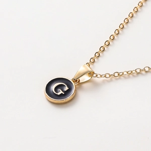 Détail d'un collier doré de 52cm avec pendentif rond en émail noir et lettre G stylisée