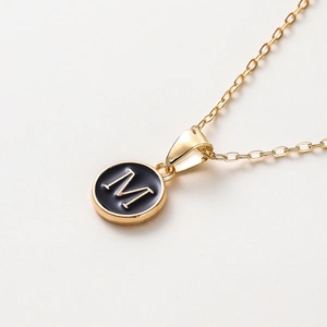 Vue macro du collier doré à maille Jaseron avec pendentif émail noir et la lettre M