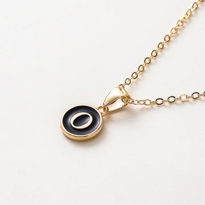 Macro d'un collier doré avec pendentif rond en émail noir et lettre O minimaliste