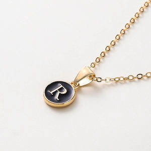 Vue macro d'un collier doré de 52cm avec pendentif en émail noir et lettre R dorée
