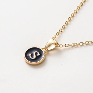 Détail du collier lettre S dorée avec pendentif en émail noir sur une chaîne fine
