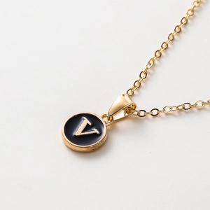 Détail d'un collier doré minimaliste avec un pendentif rond lettre V en émail