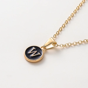 Vue macro de la chaîne dorée et du pendentif en émail noir avec la lettre dorée W