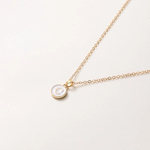 Détail du collier doré avec pendentif lettre C sur un médaillon rond blanc élégant