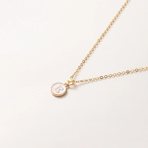 Détail macro du collier doré avec pendentif lettre E en émail blanc sur chaîne fine