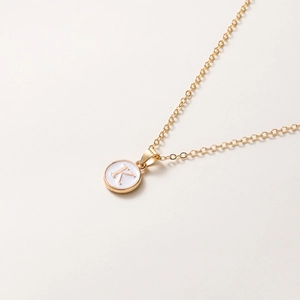 Détail du collier chaîne dorée avec pendentif rond blanc orné de la lettre K gravée