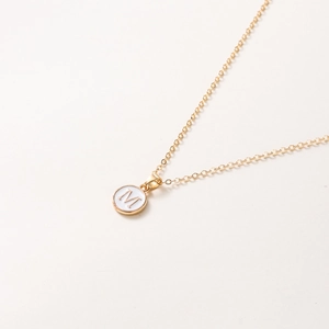 Détail du collier doré de 52cm avec pendentif lettre M sur une surface beige neutre