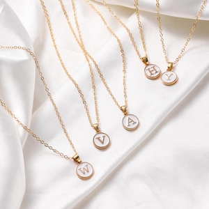 Cinco collares dorados con letras sobre fondo de seda blanca con colgantes redondos de esmalte
