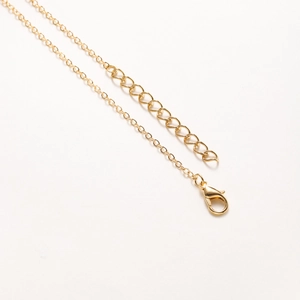 Collier doré avec fermoir mousqueton réglable et chaîne d'extension sur fond blanc minimaliste