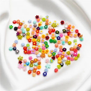 Detalle de pequeñas flores de resina de 6mm de colores para DIY sobre satén blanco