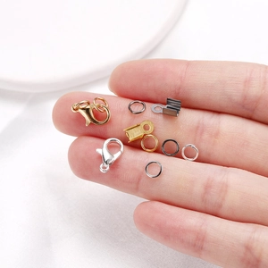 Macro view of tiny lobster clasps and jump rings held on a finger for size scale
