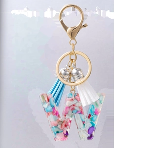 Détail d'un porte-clés lettre W en résine avec pierres colorées, fermoir doré et glands