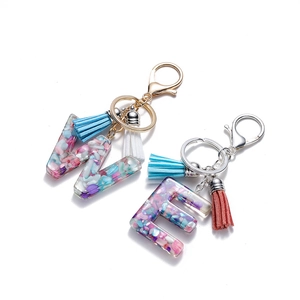 Vue détaillée de porte-clés alphabet en résine avec paillettes colorées et pompons en cuir