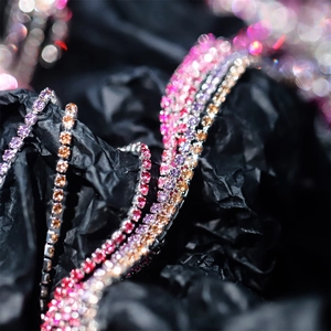 Macro shot of colorful 2mm rhinestone claw chains in pink, purple and red on black background