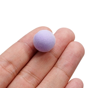 Vue détaillée de la perle floquée violette tenue par les doigts montrant sa texture velours