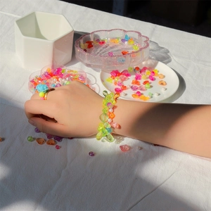 Detail of colorful Y2K resin bead bracelet and blue flower ring worn by a child
