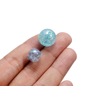 Detailed macro view of 16mm crackle acrylic beads held on finger for scale