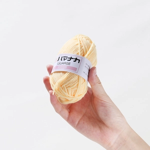 Close-up of pale yellow 4-ply milk cotton yarn with brand paper sleeve held in hand
