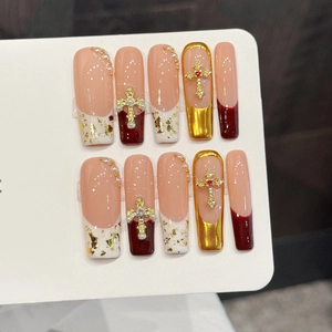 Pink and burgundy press-on nails with gold accents and 3D metallic cross charms