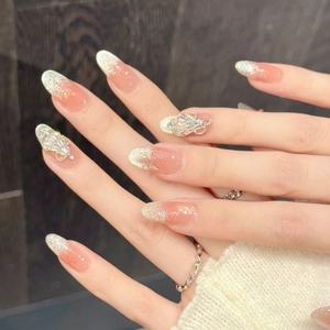 Pink gradient glitter press-on nails with 3D rhinestone accents in oval shape on wood