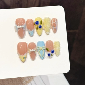 Pink and yellow press-on nails with 3D bows, blueberry charms, and floral art
