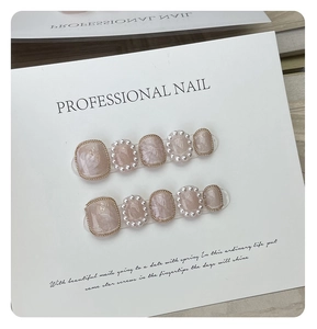 Detailed view of handmade pink pearl press-on nails with gold trim and white pearl accents