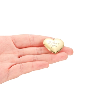 Polished gold heart locket pendant with I Love You engraving held in palm on white background