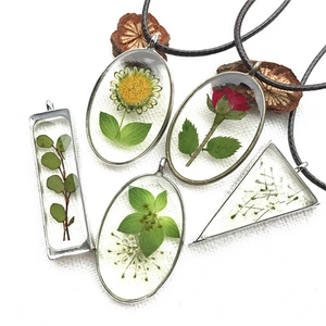 Dettaglio macro di ciondoli geometrici in resina con fiori secchi e cordini neri