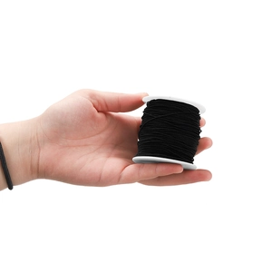 Elastic black beaded cord roll on white spool for jewelry making shown in hand for scale