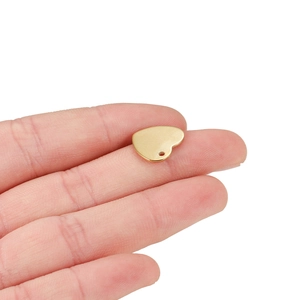 Close-up of a tiny gold heart pendant on a fingertip showing its mini size and hole