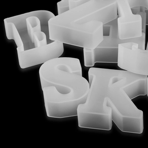 Close-up of translucent white silicone 3D letter molds B, S, and R on a black background