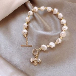 Perlenarmband mit goldenem Bienenanhänger und OT-Verschluss auf grauem Seidenhintergrund